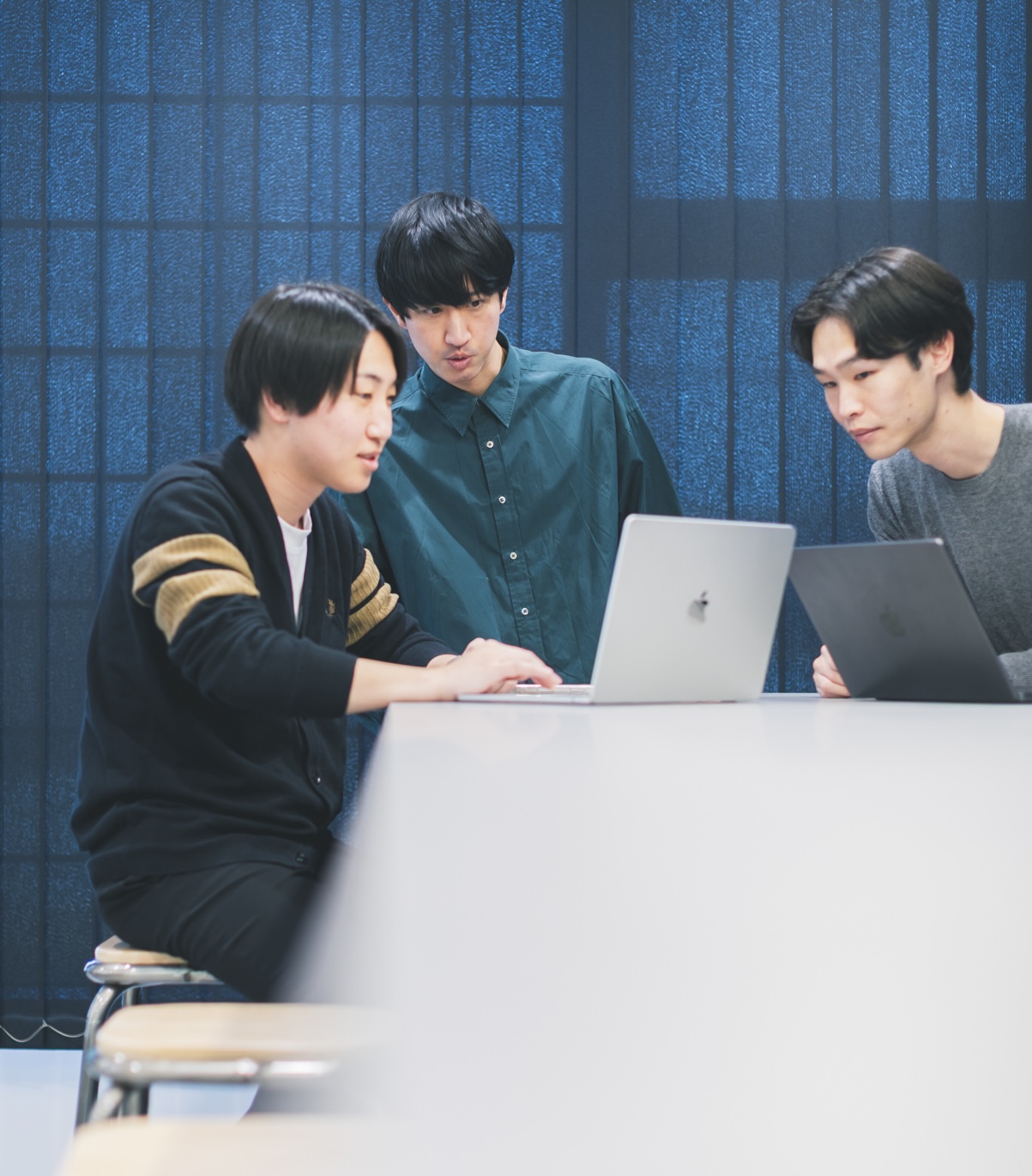 3人のメンバーがノートPCを見ながら議論する様子